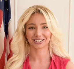 Andrea Catsimatidis, smiling, in pink, an American flag behind her