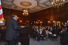 A speaker at the lectern, seen from behind, facing the dining room
