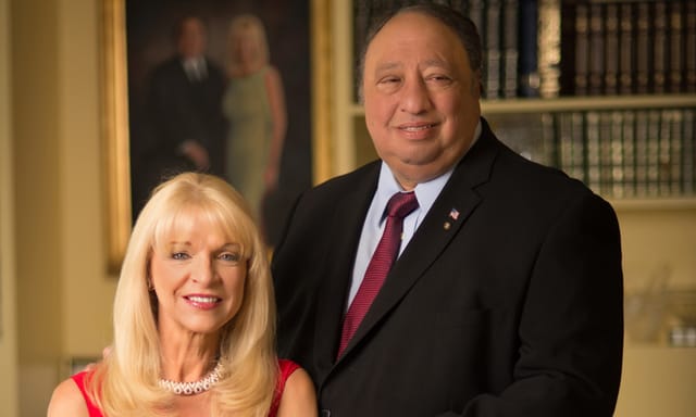 John and Margo Catsimatidis in a library, a painted portrait of the couple behind them