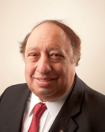 John Catsimatidis, smiling, in a dark suit, white shirt and red tie